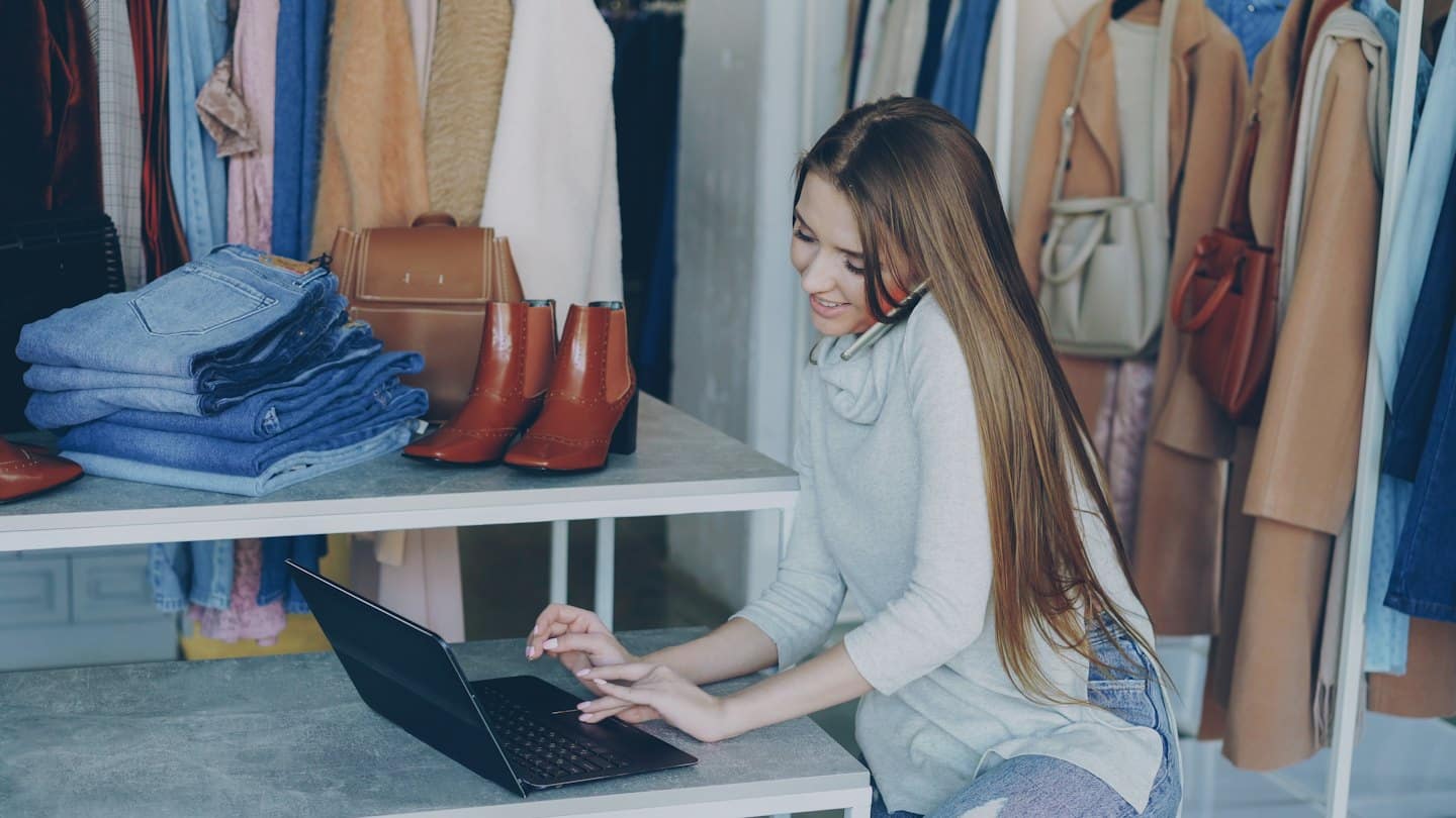 Donna lavora al computer in un negozio di abbigliamento con scaffali di vestiti.